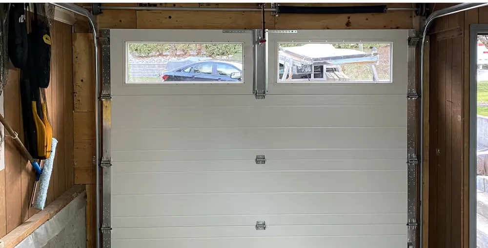 Inside the same garage, a new white ribbed garage door with two windows along the top