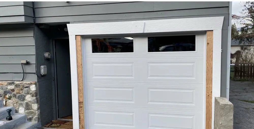 A white raised-panel garage door with two top windows, bare wood jambs showing at the sides