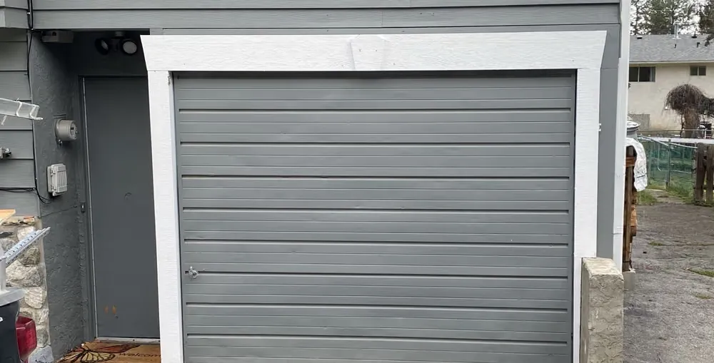 A grey horizontally ribbed garage door framed in white trim on a grey-sided home