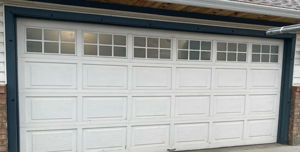 A white double garage door with a row of grid-pane windows and short raised panels, framed in dark blue trim