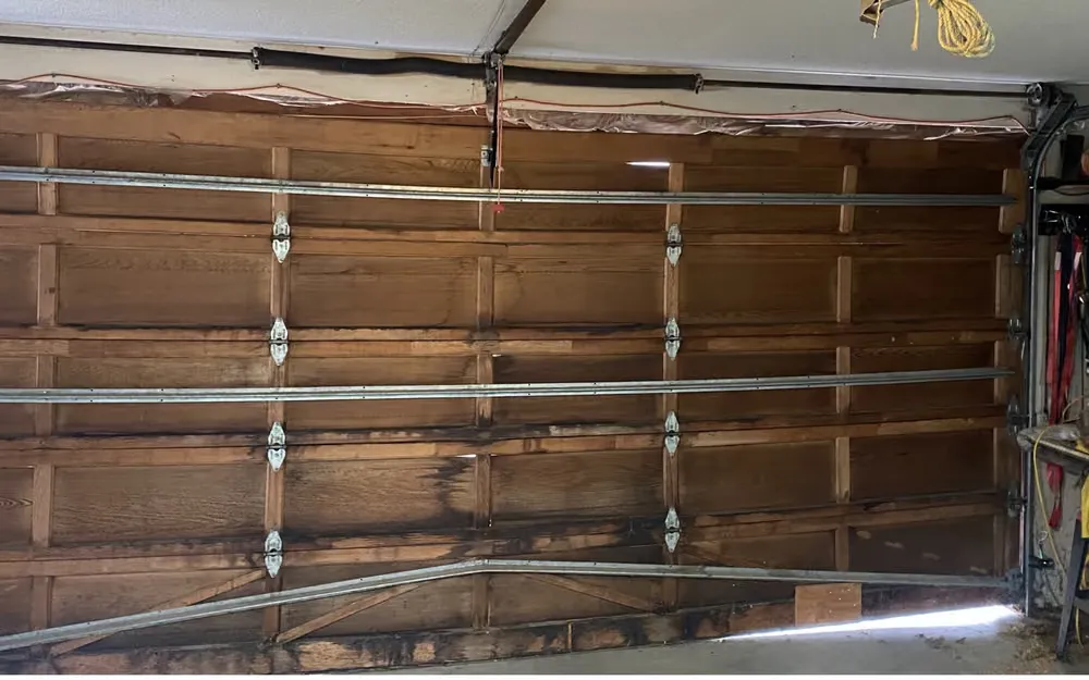 Inside a garage, an old wooden door braced with steel struts, water-stained along the bottom with daylight showing underneath