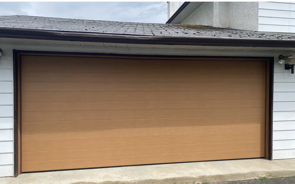 A wood-grain flat-panel double garage door in a warm cedar tone on the same home