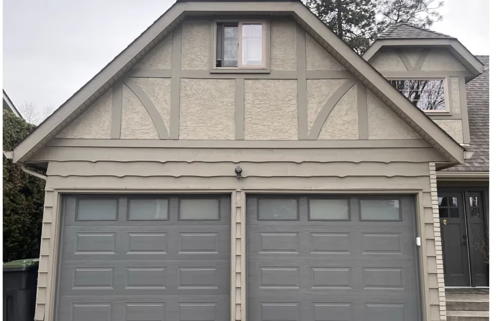 Two grey garage doors with top windows under the same half-timbered gable