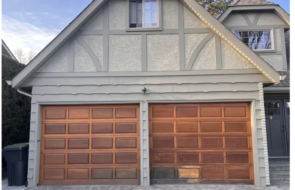Two stained wood raised-panel garage doors under a half-timbered stucco gable