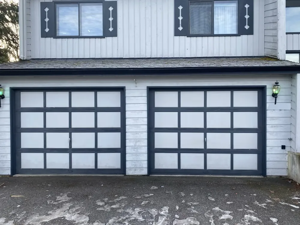 Two dark-framed garage doors with a grid of white panels on a white-sided home