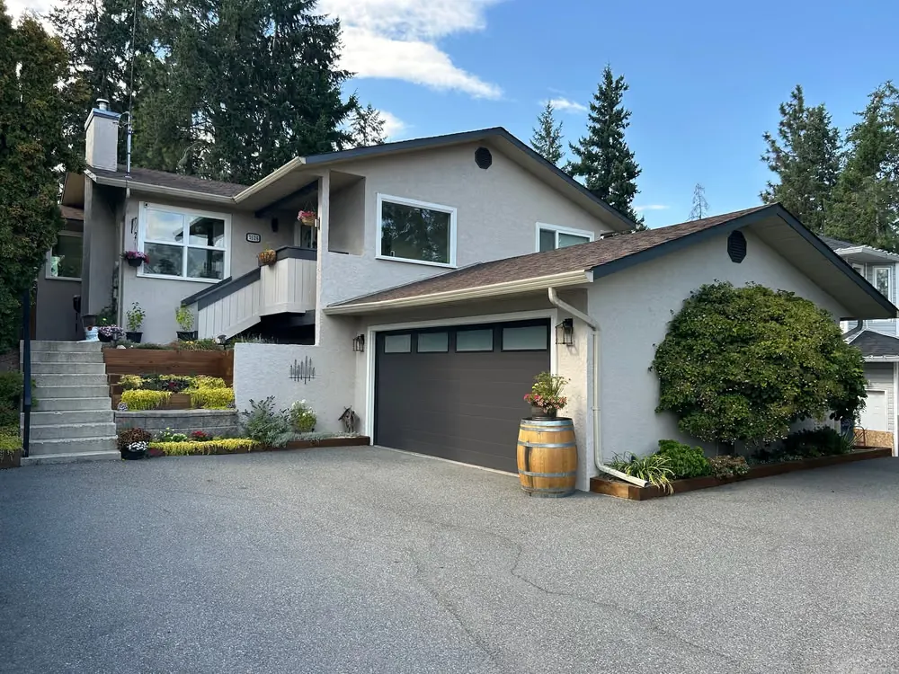 The same home now painted grey, with a dark garage door with top windows and a wine barrel planter beside it