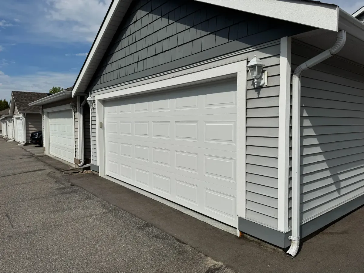 A white raised-panel garage door installed on a grey-sided Okanagan home