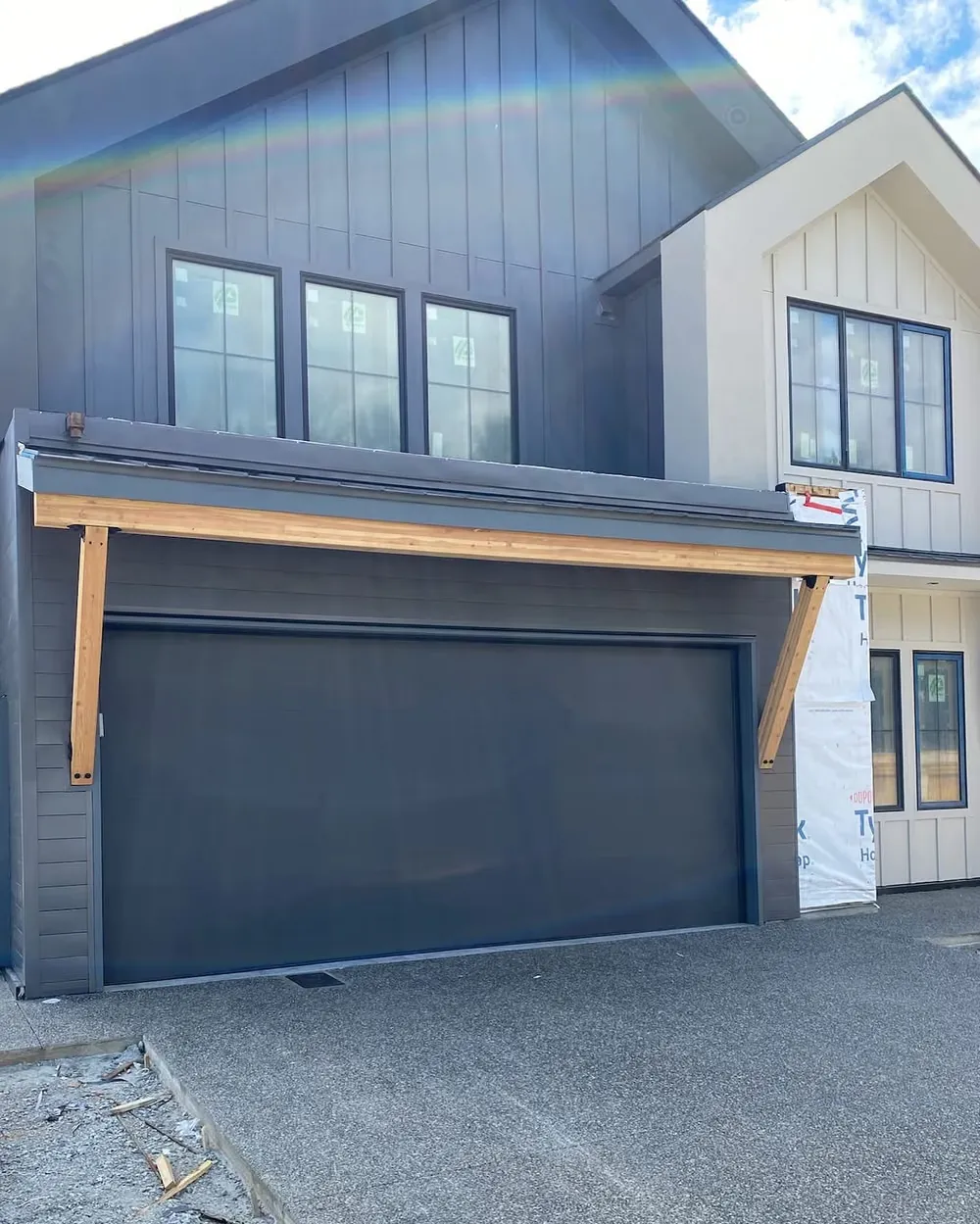 A dark garage door under a timber beam on a white board-and-batten home