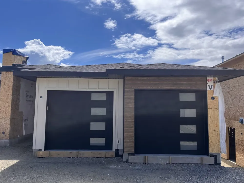 Two black flush garage doors with vertical window strips on a home still under construction