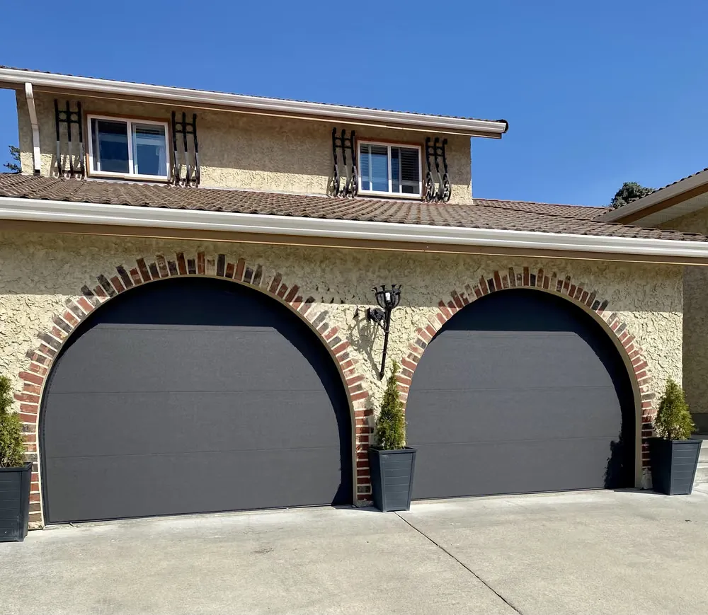 Two dark garage doors set into brick archways on a stucco home with wrought-iron balconies