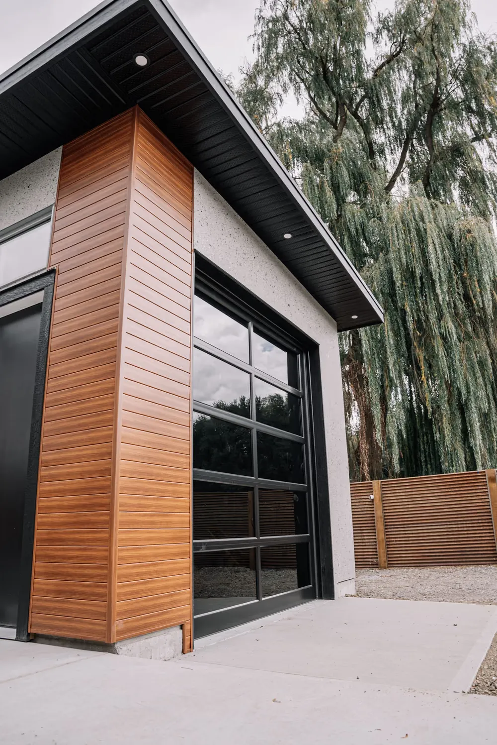 A modern shop with a black full-view glass garage door and a horizontal cedar-clad corner