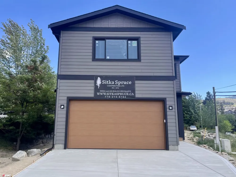 A wood-look garage door on a tall grey shop with a Sitka Spruce sign above the opening