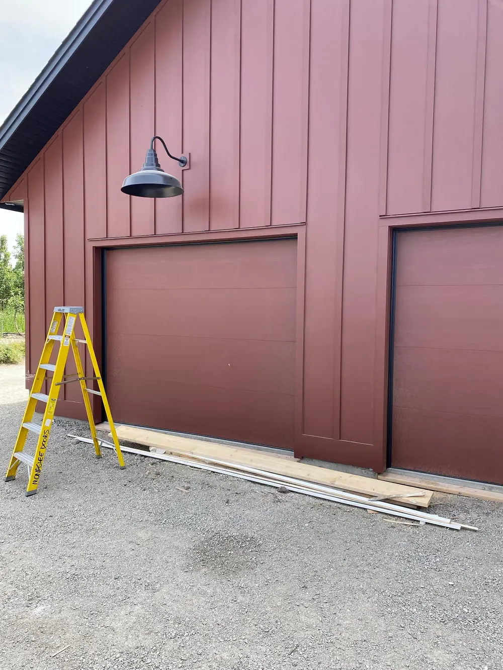 Two tall garage doors on a red barn-style shop, with a ladder set up for the install