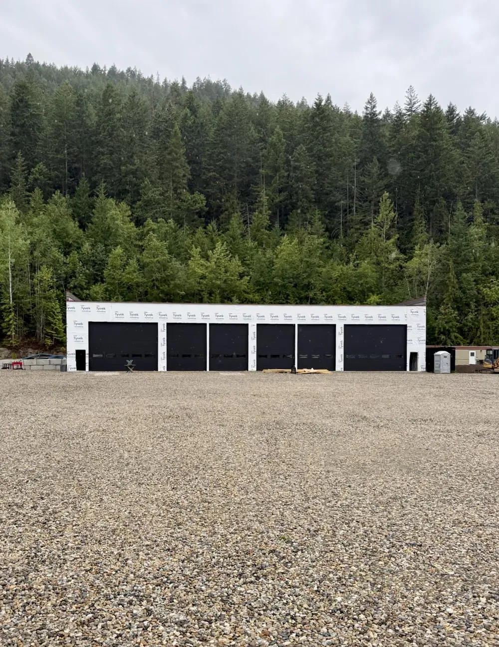 A long row of black garage doors on a storage building backed by forest