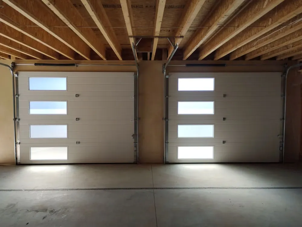 Two white garage doors with frosted window strips, seen from inside a garage with exposed ceiling joists