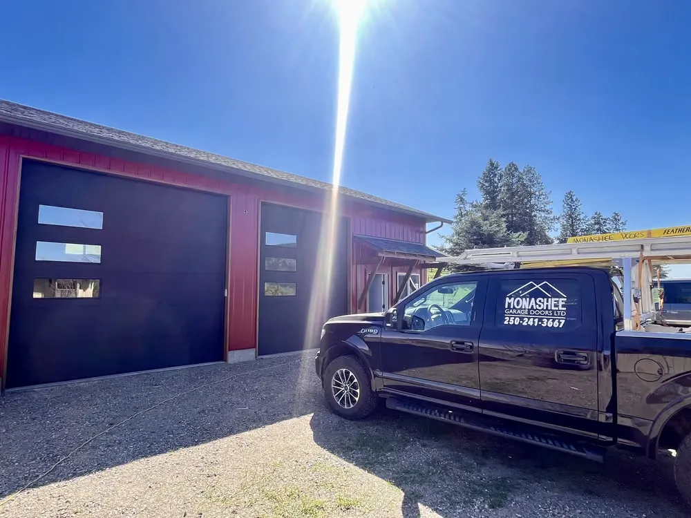 A Monashee truck parked at a dark red shop with a new black garage door, shot into the afternoon sun