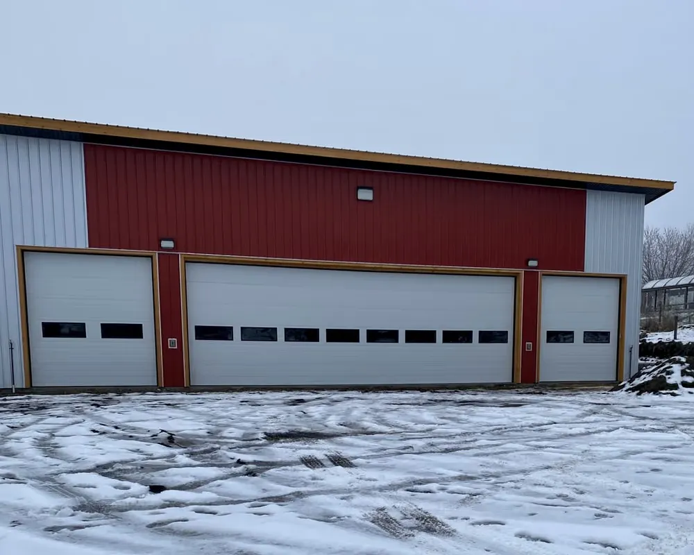 A row of white commercial overhead doors on a red steel shop with snow on the ground