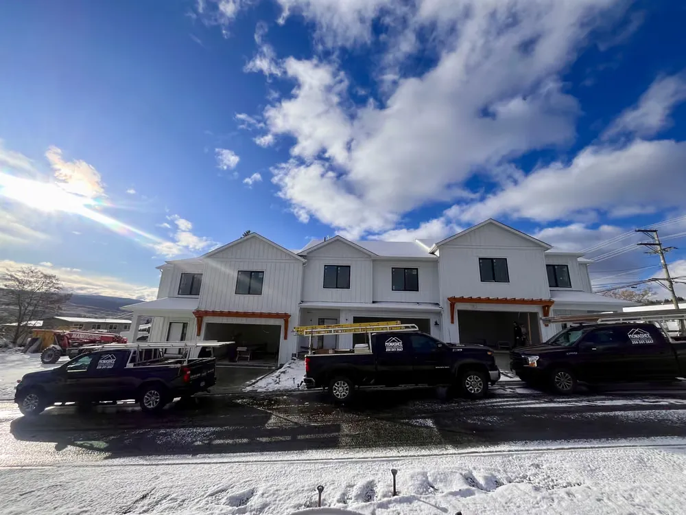 New townhomes with their garage doors going in and crew trucks parked out front on a winter morning