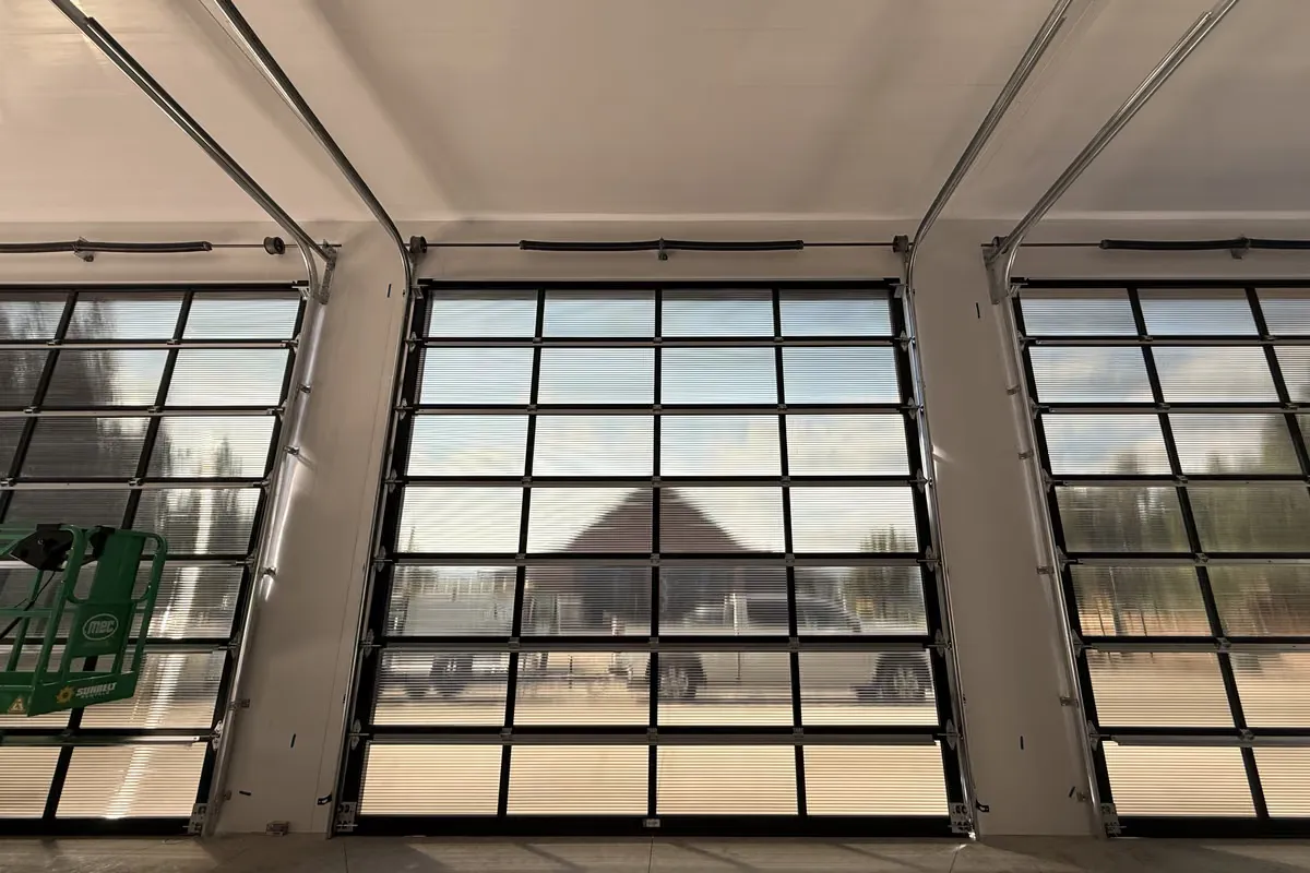 Three full-view glass garage doors seen from inside a large new building, an aerial lift parked at left