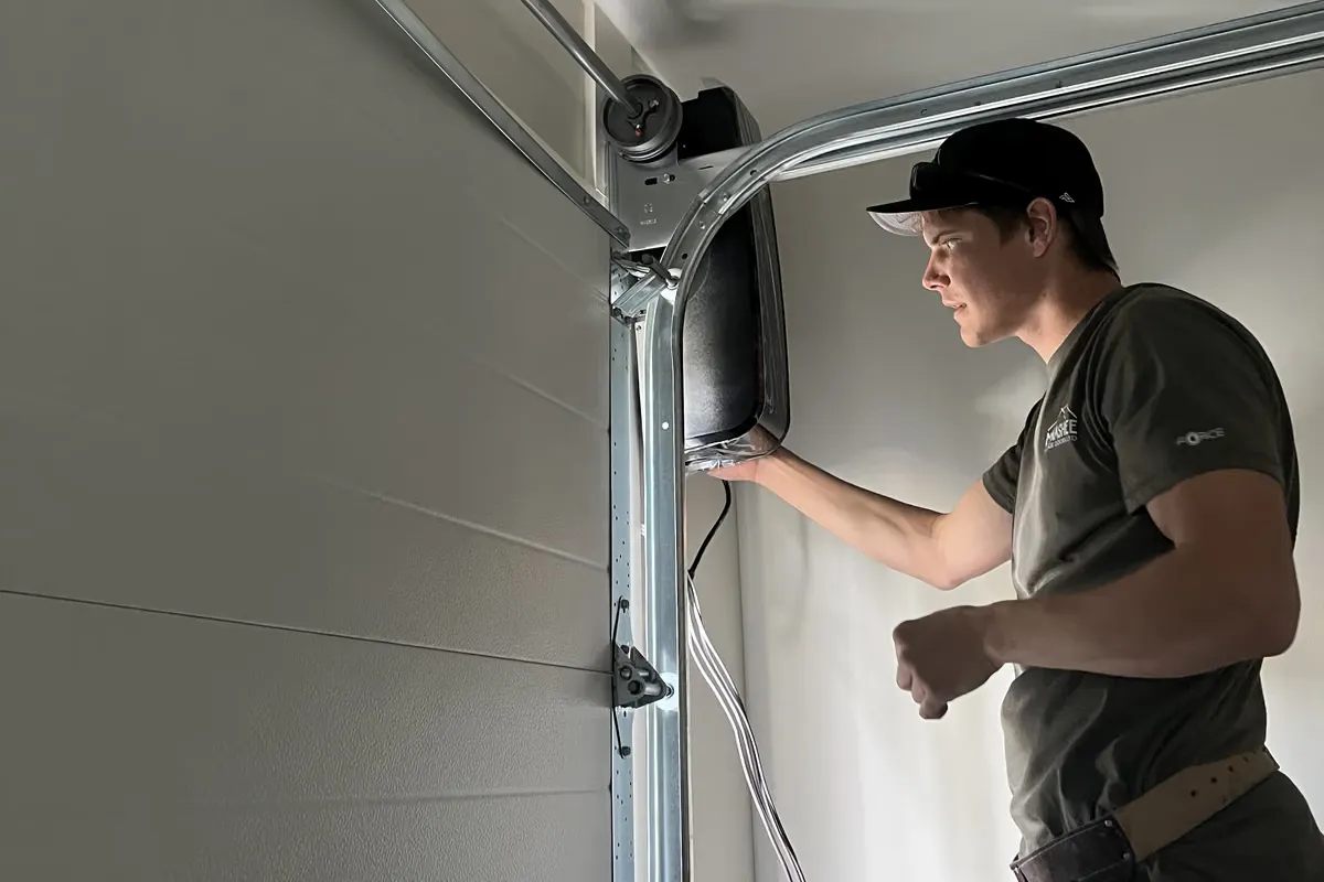 A technician in a Monashee shirt works on a wall-mounted opener beside the garage door track