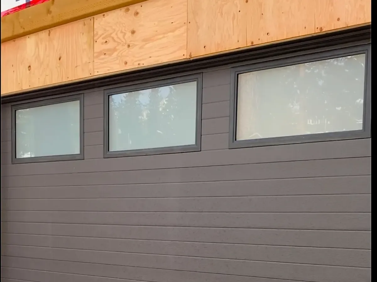 A brown garage door with three frosted windows on a new build
