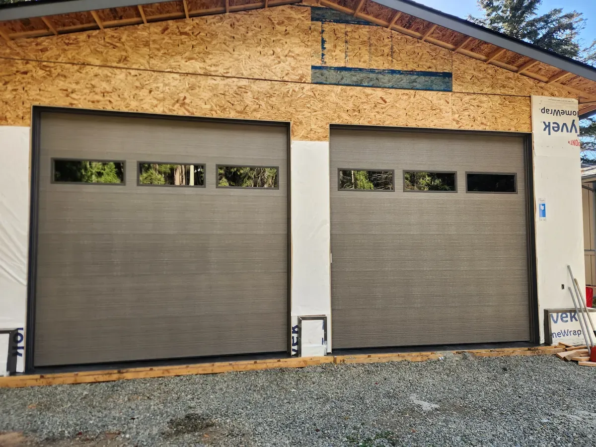 Two grey woodgrain garage doors installed on a garage still under construction