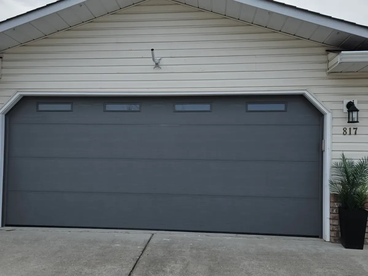 A charcoal garage door with four top windows on a cream-sided home